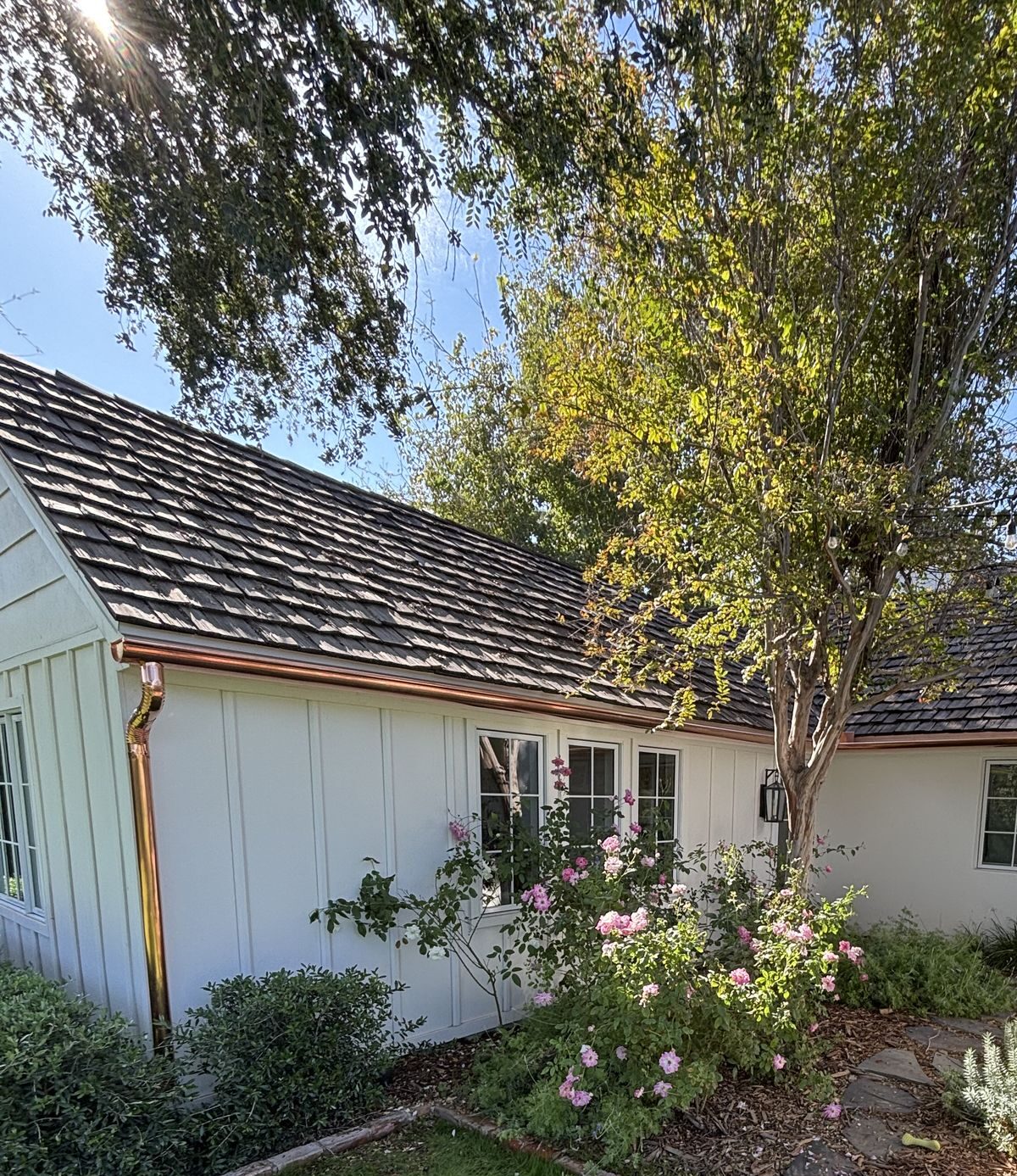 Copper gutter and decorative downspout on white board-and-batten home with garden — Grizzly Rain Gutters