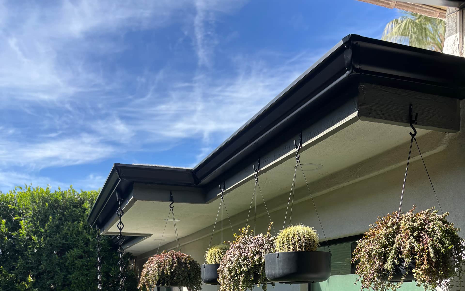 Copper rain chains channeling water over landscaping at a Phoenix-area home by Grizzly Rain Gutters